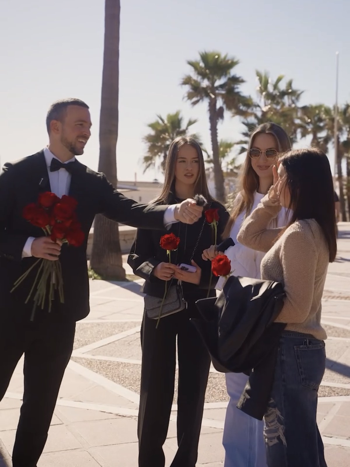 A man in a tuxedo handing out red roses to smiling passers-by on the Marbella promenade