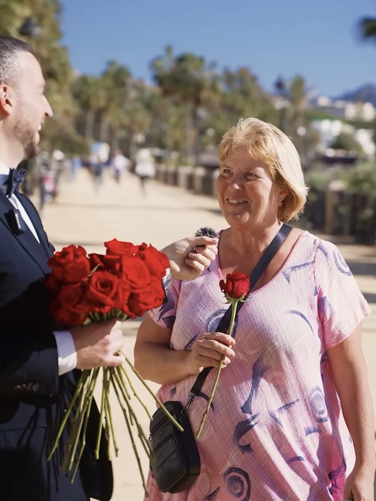 A woman receiving a single red rose and smiling during a spontaneous street interview