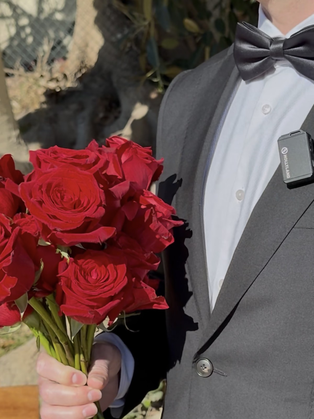 Close-up of a bouquet of red roses held by a man in a tuxedo with a wireless microphone