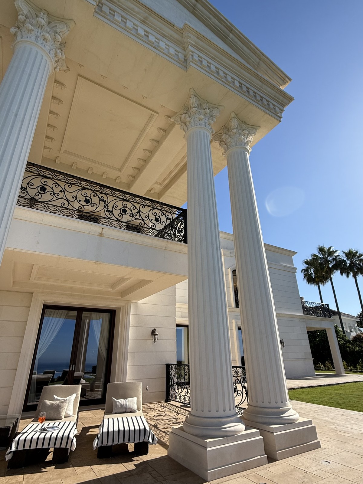 The villa's classical portico with fluted Corinthian columns and striped sun loungers overlooking the sea