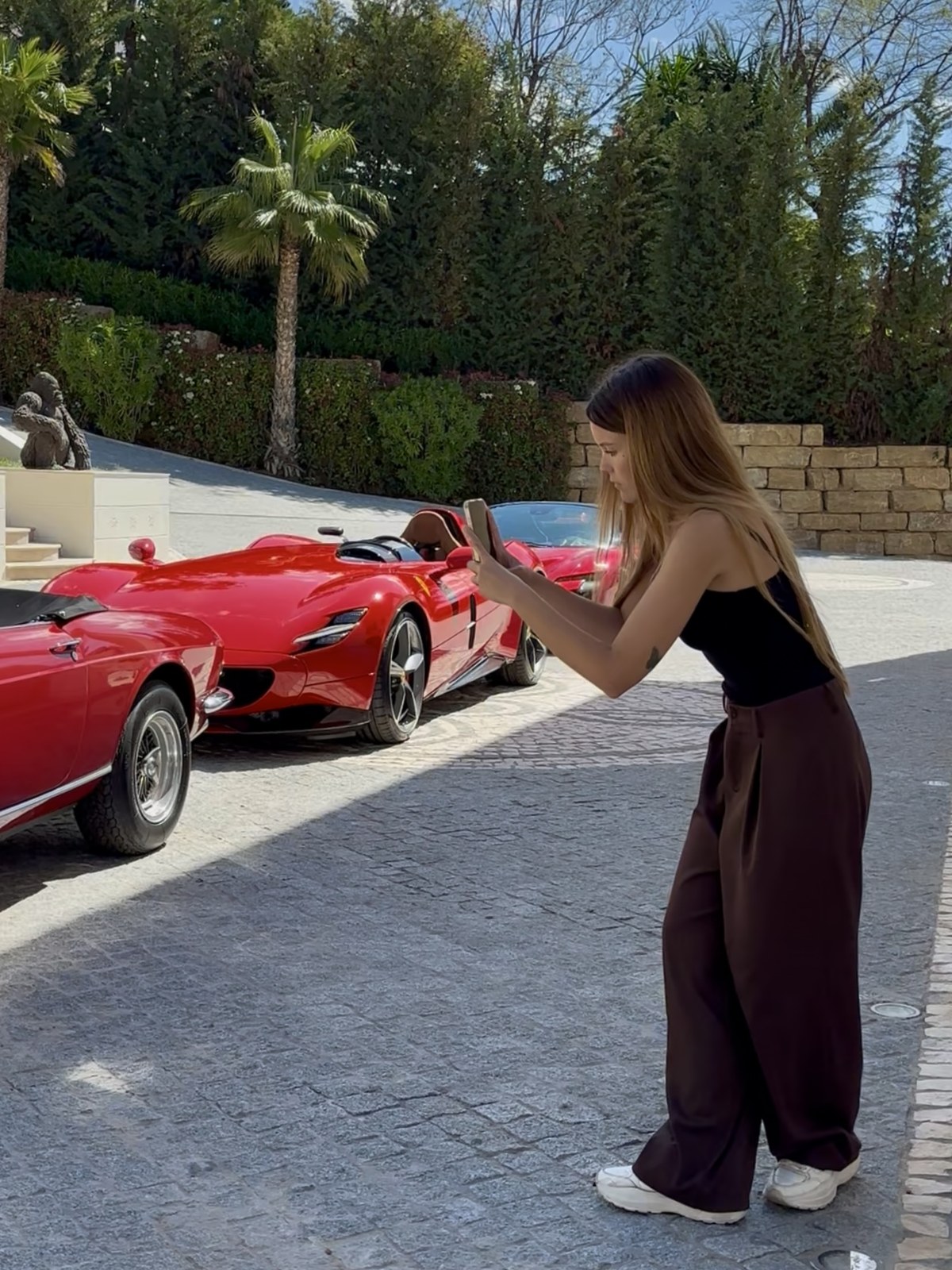 Savannah filming a red Ferrari on her phone in the villa driveway during production